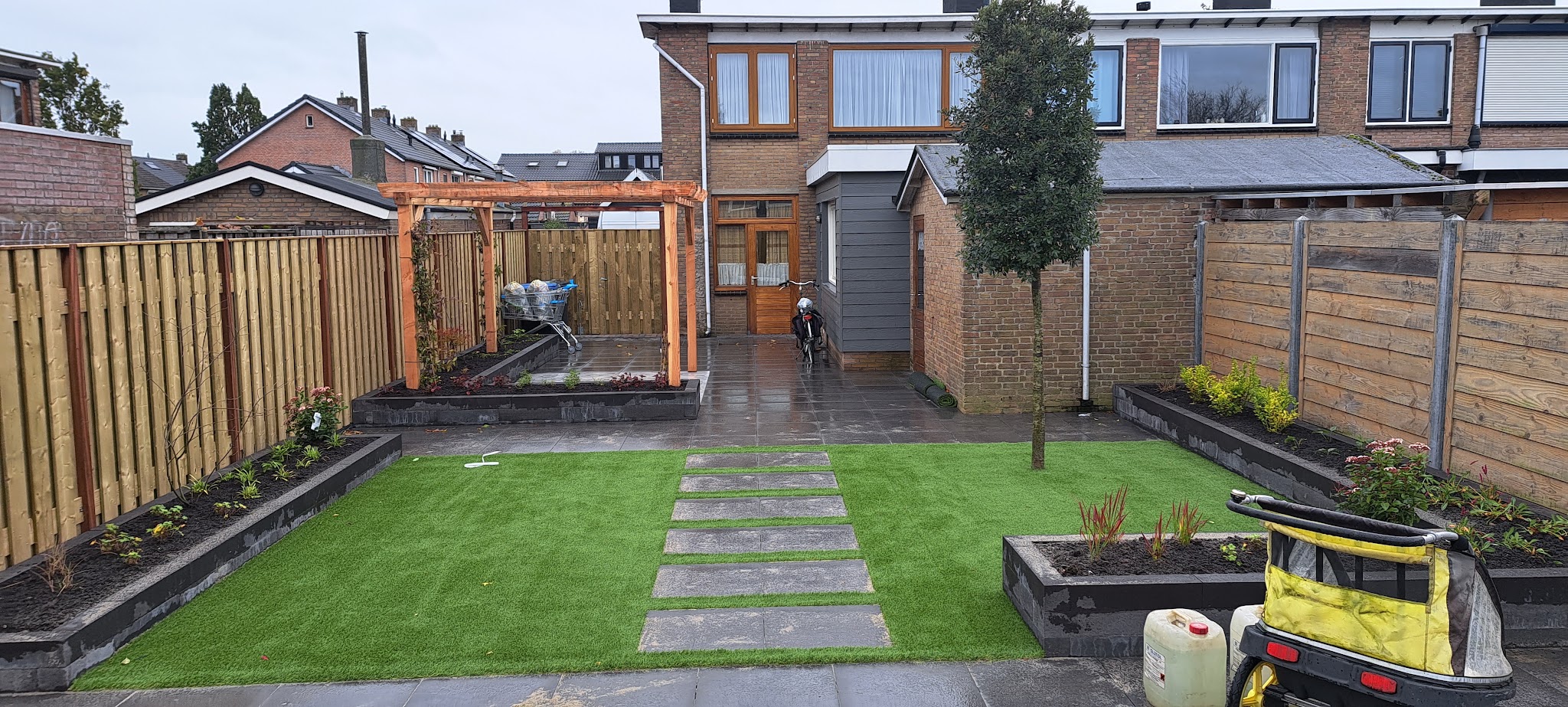 Aangelegde achtertuin met stapstenen door het gras, verhoogde borders en een pergola