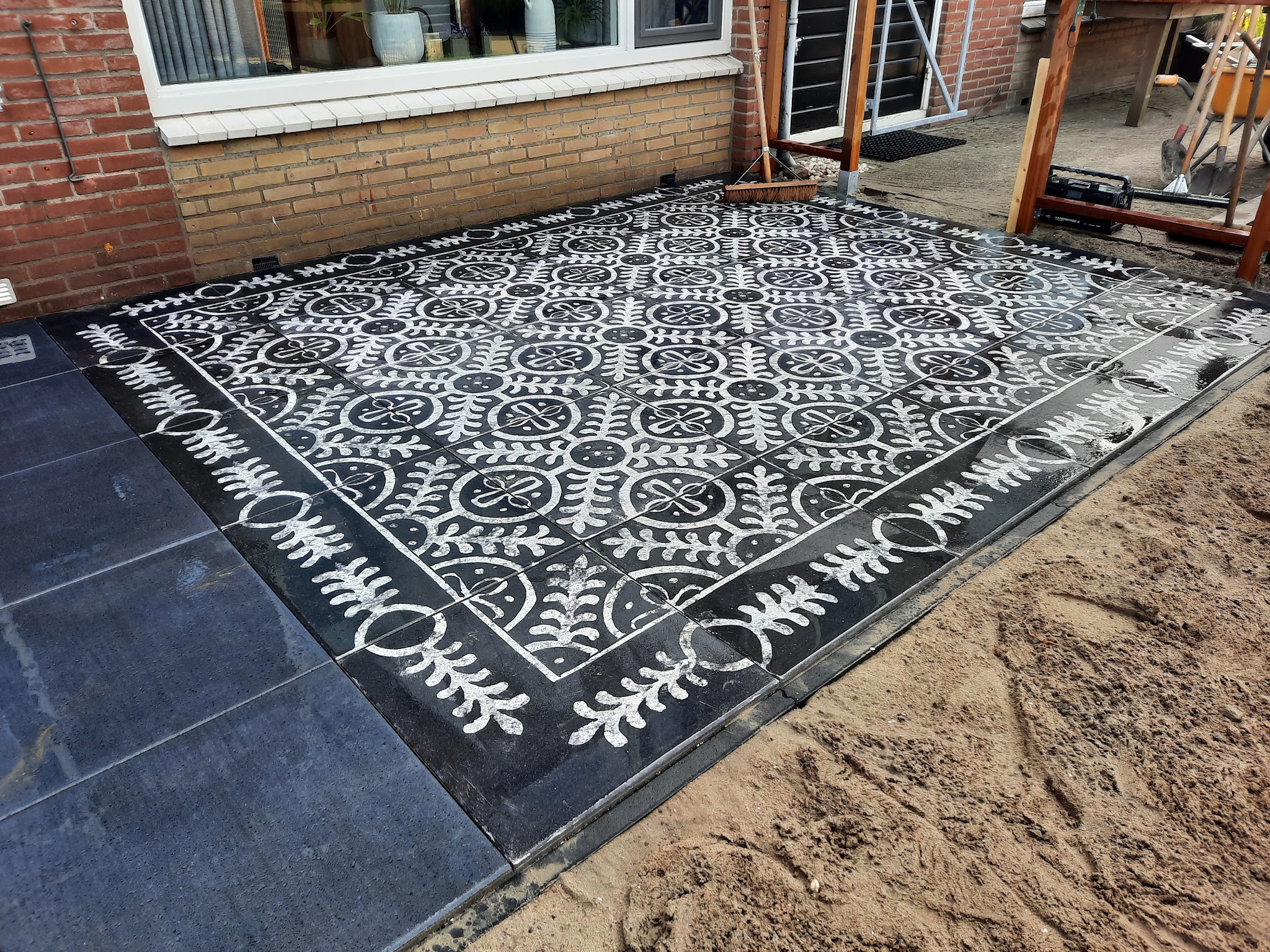 Terras met zwart-wit patroontegels en een donkere rand, gelegd in het zand