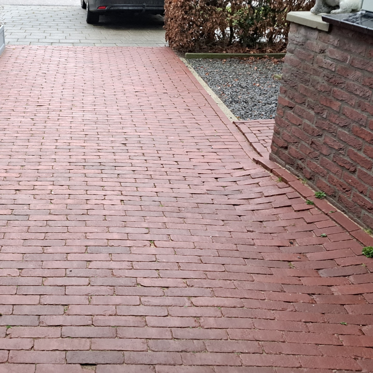 Pad van rode gebakken klinkers langs een gemetselde plantenbak