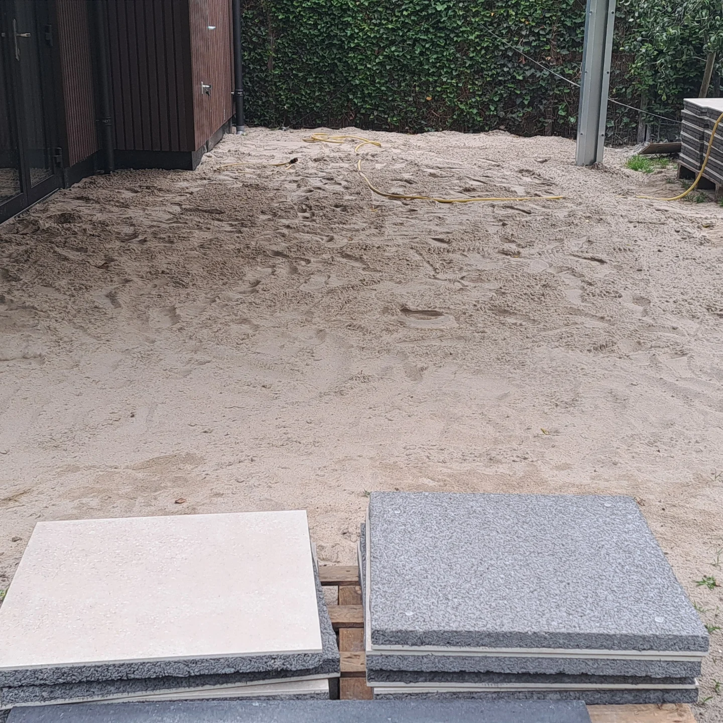 Proeftegels in beige en graniet-look op een geëgaliseerd zandbed